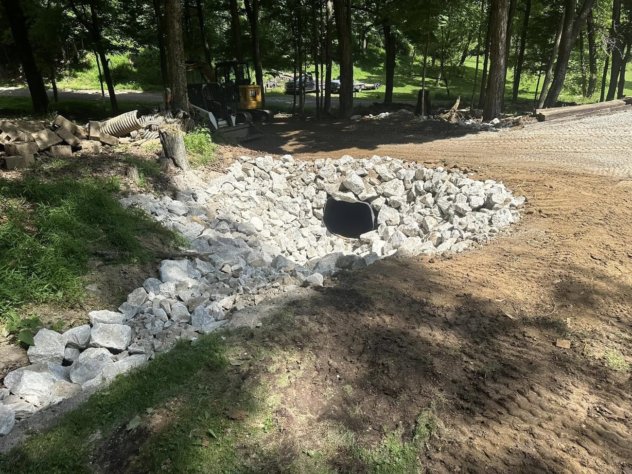 Culvert inlet armored with heavy stone beside the finished drive, skid steer parked behind