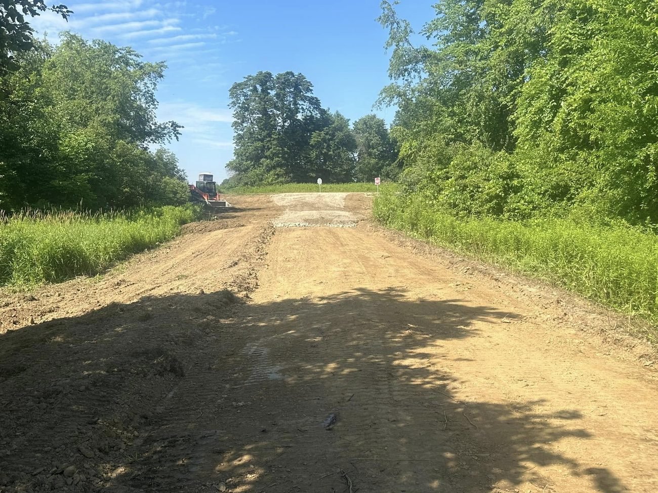 New farm lane being cut and shaped through brush with a skid steer working at the top of the rise
