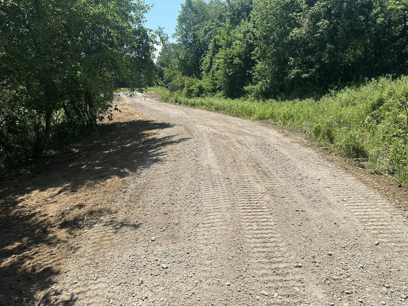 The same farm lane finished with a crowned gravel surface running between cleared brush lines