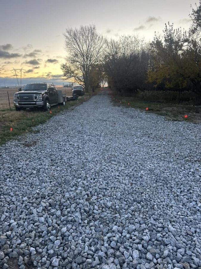 Freshly laid white limestone driveway at dusk with orange marker flags along both edges and a truck and trailer parked at the side