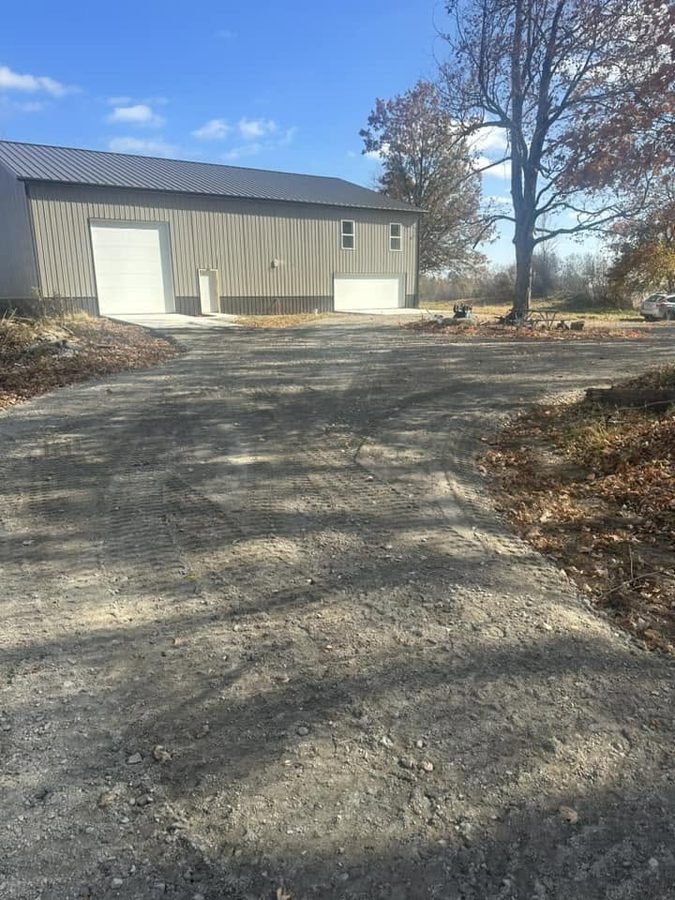 Graded gravel drive and turnaround apron leading up to a tan pole barn with two overhead doors